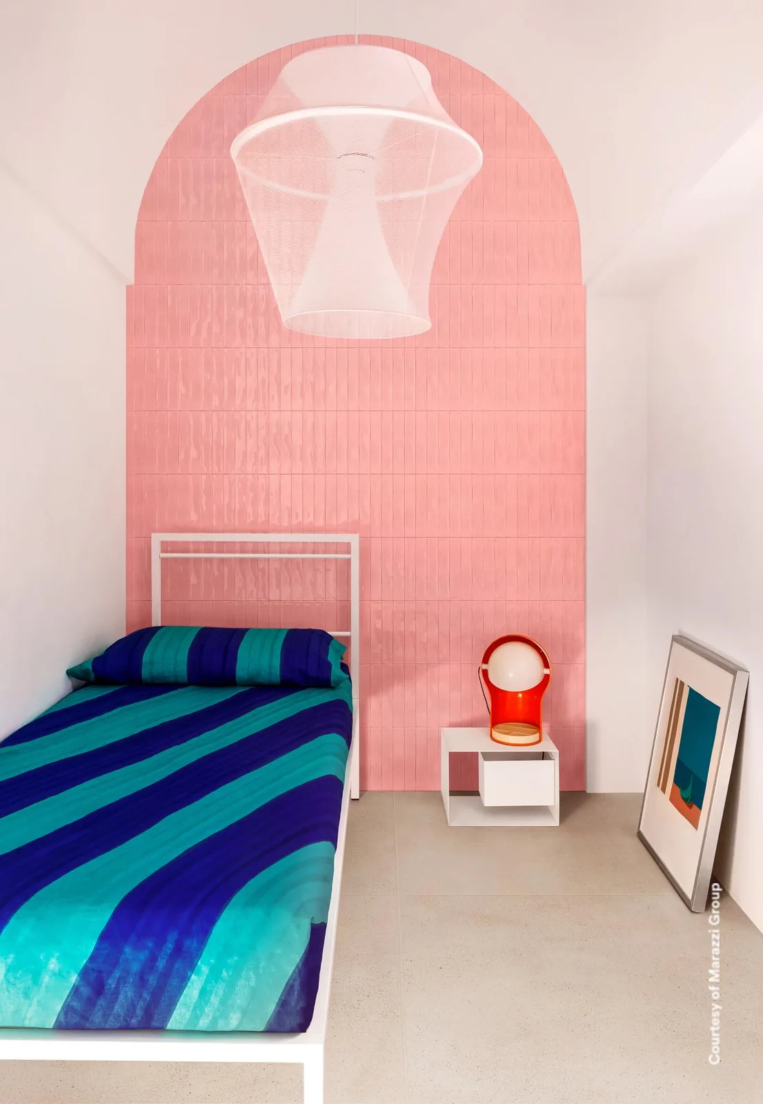 Bogen aus rosa Glanzriemchen als Kopfteil hinter einem Bett mit blau gestreifter Decke, darüber eine Leuchte