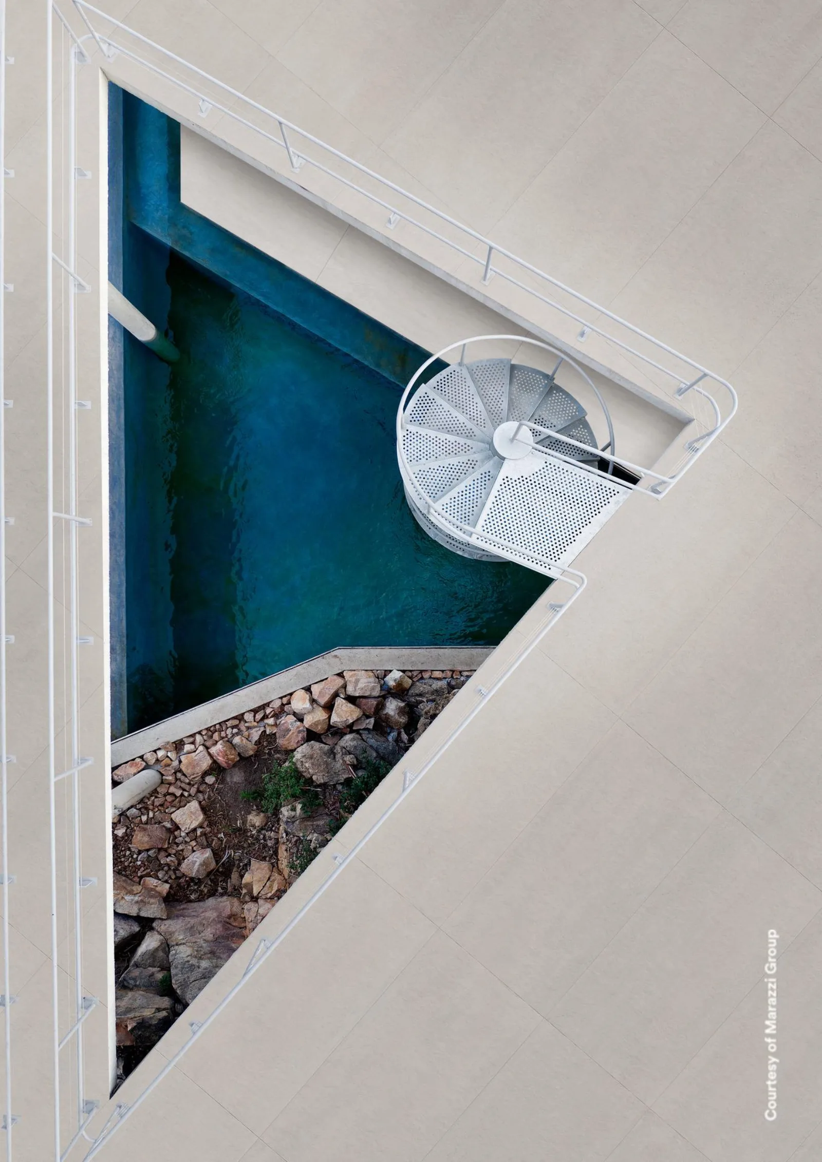 Blick von oben auf einen Innenhof mit Pool und Wendeltreppe, Boden aus beigegrauen Betonoptik-Fliesen.