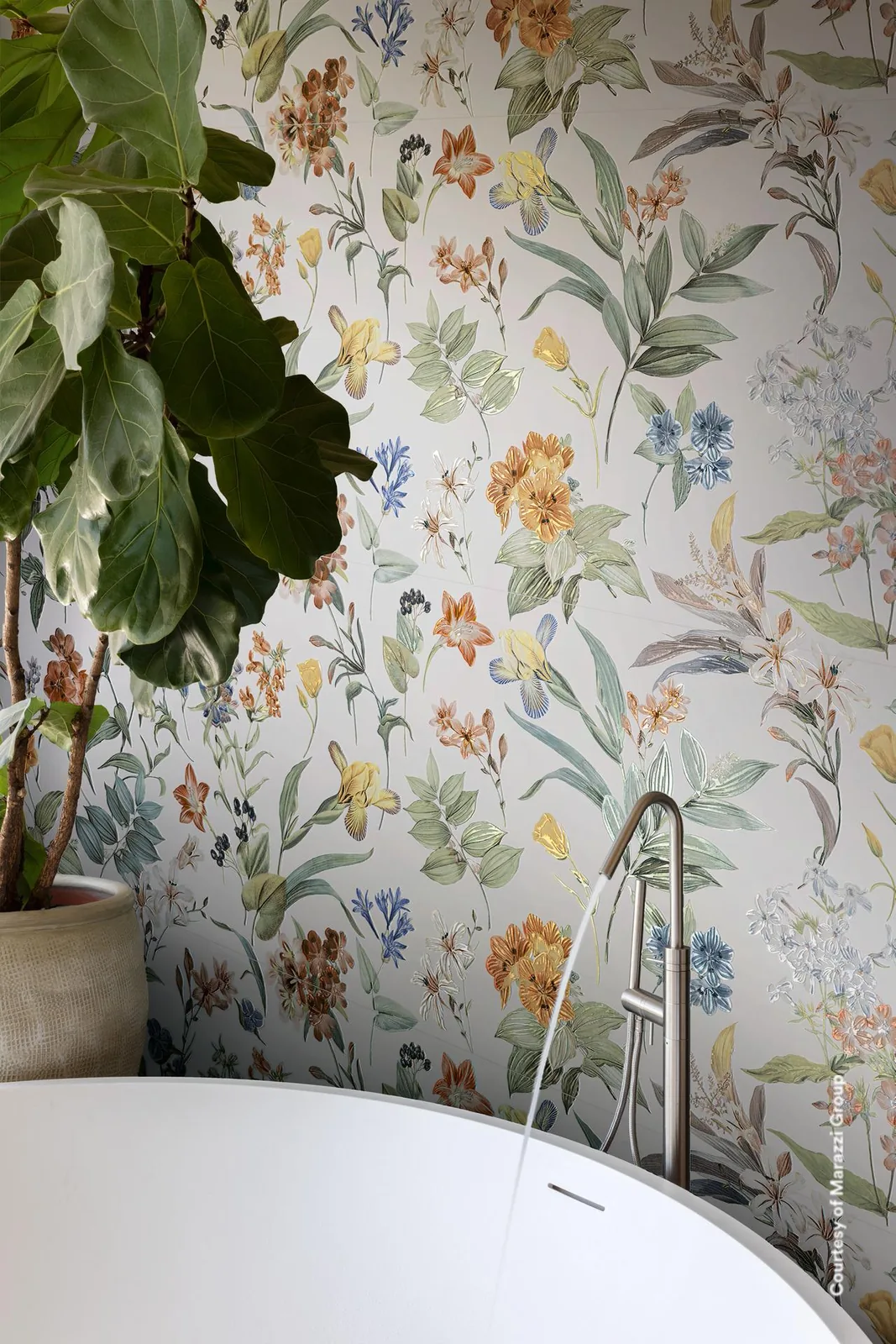 Freistehende Badewanne mit Standarmatur vor einer Wand mit bunten Wildblumen auf weißem Grund, links eine Grünpflanze.