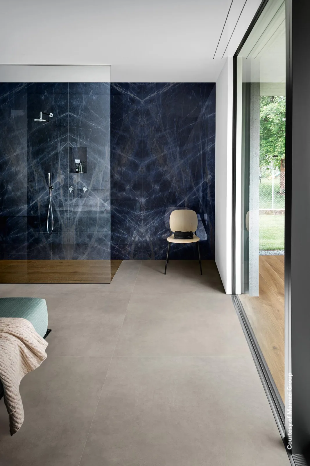 Offenes Bad mit Duschwand in tiefblauer Marmoroptik, spiegelbildlich verlegt, grauer Boden und Glasfront.
