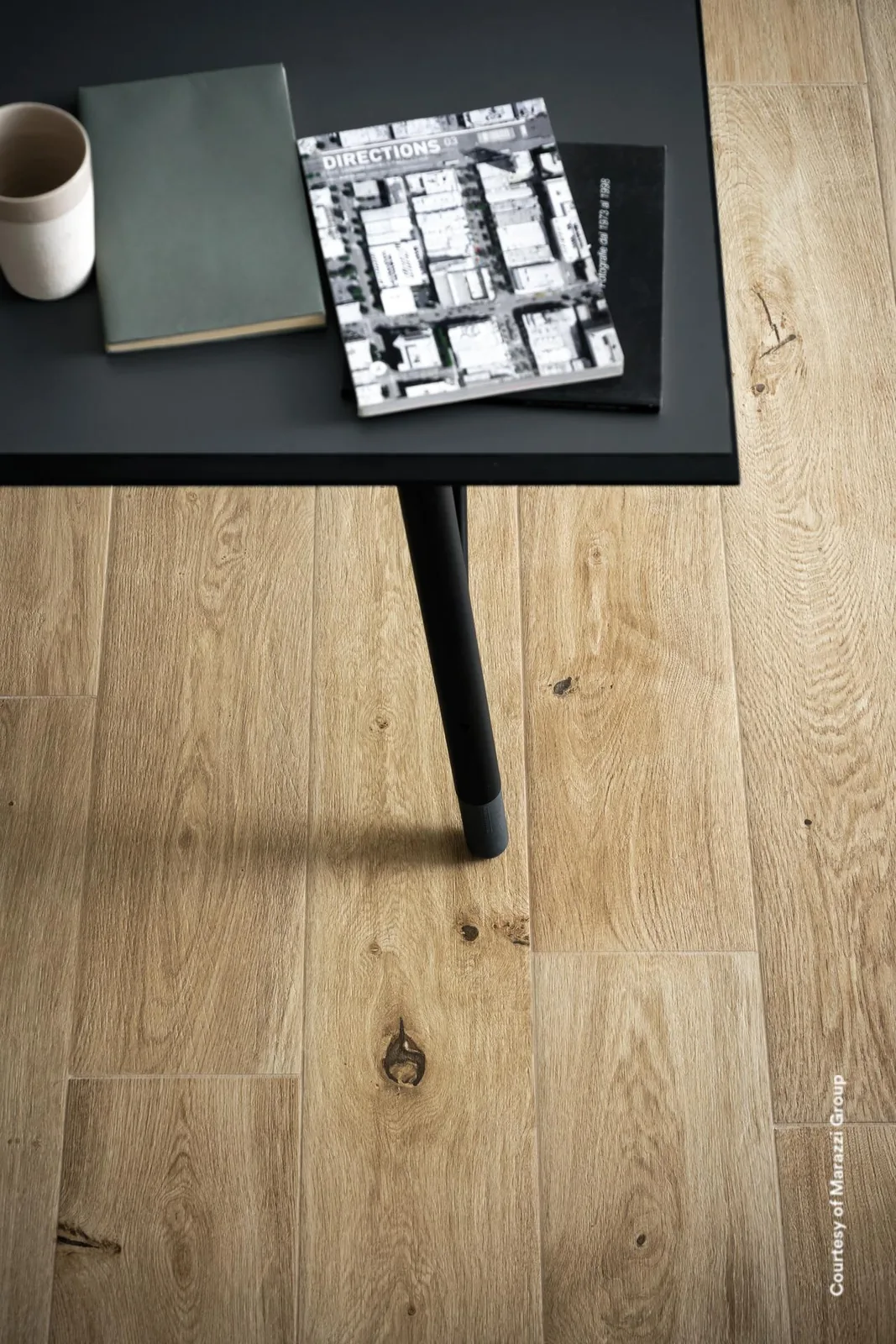 Nahaufnahme naturbeiger Holzoptik-Dielen mit Astlöchern, darauf ein schwarzer Tisch mit Notizbuch und Becher.