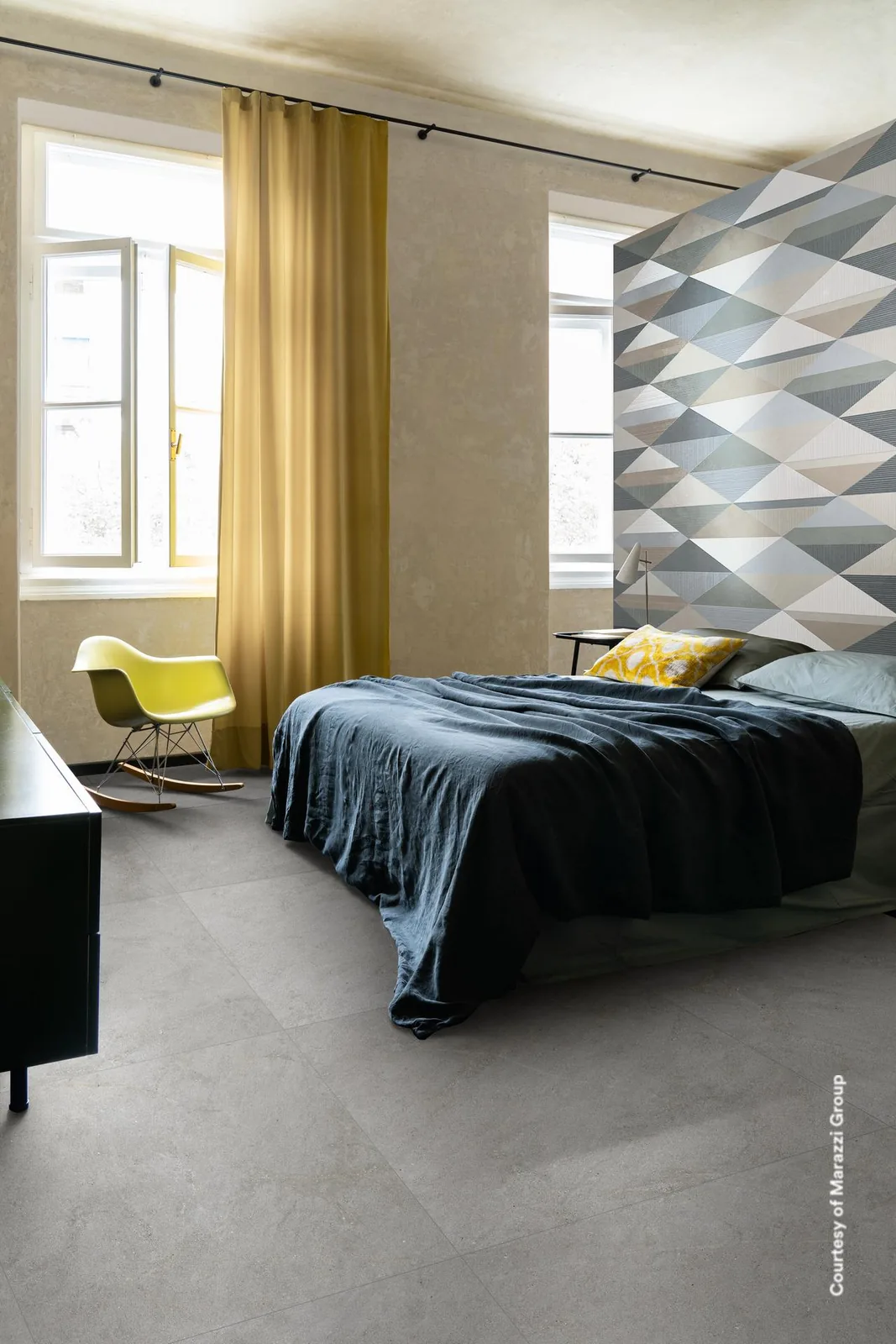 Schlafzimmer mit Bett und gelbem Vorhang, rechts eine Wand mit Dreiecksmuster in Grau, Blau und Weiß.