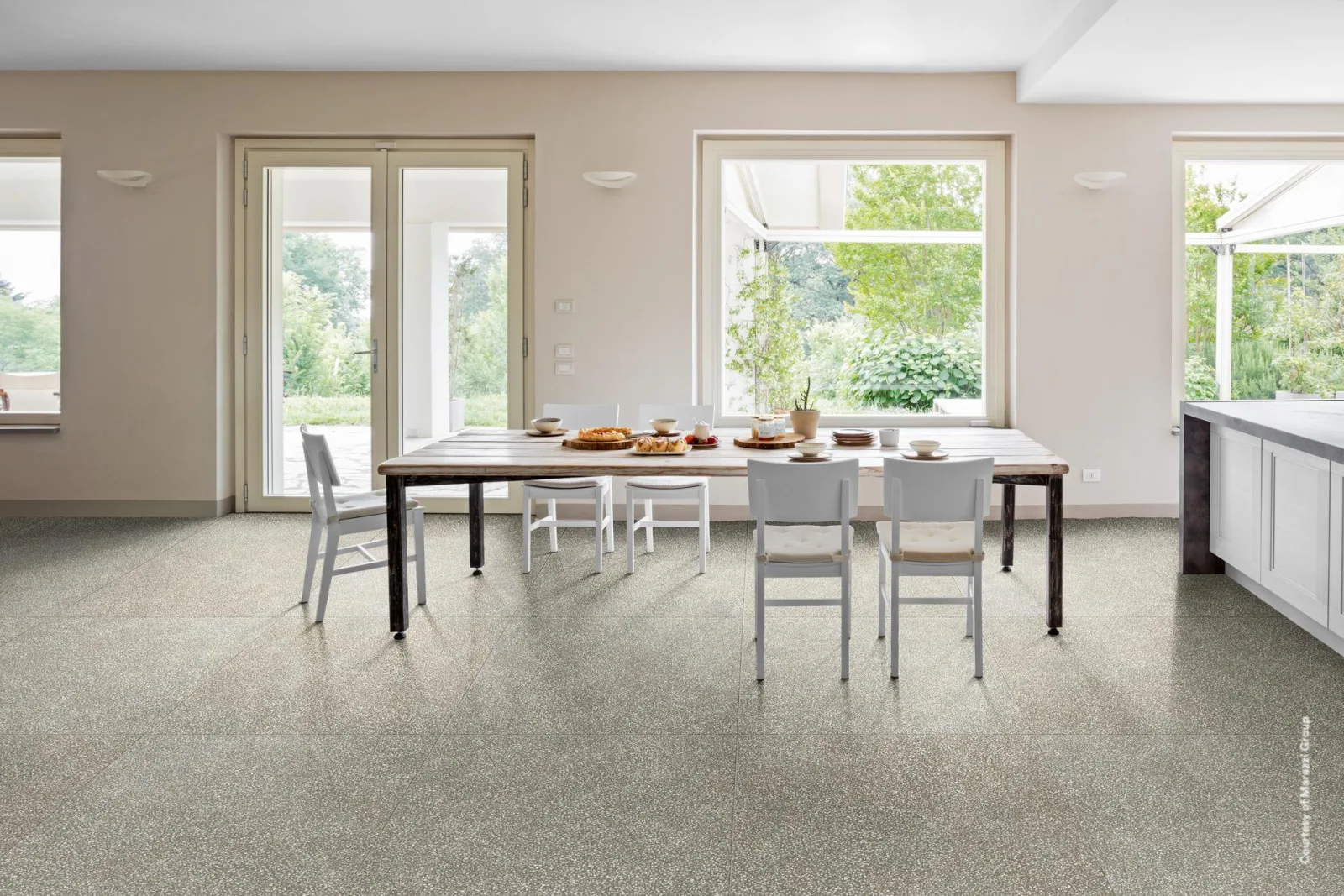 Heller Essraum mit langem Tisch und bodentiefen Fenstern zum Garten, cremeweißer Terrazzo-Boden mit feinen Splittern.